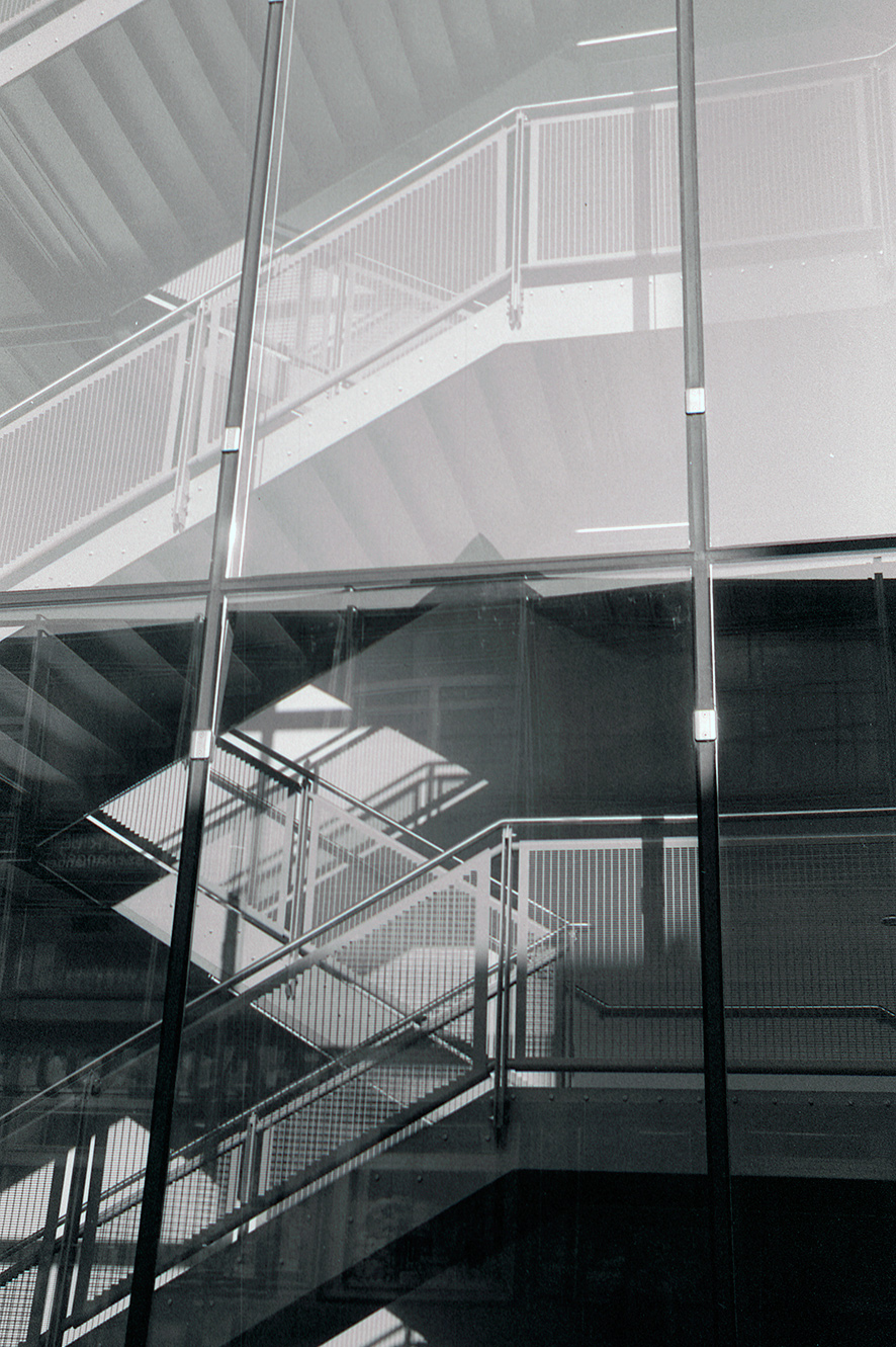 metal stairs behind a glass facade, shown in black and white.