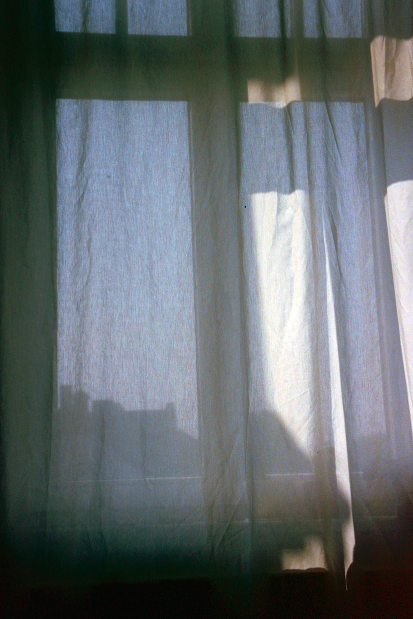 view from inside through a bright curtain, revealing the faint outlines of a building outside the window.
